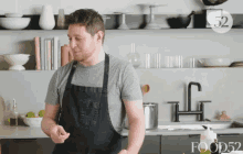 a man in an apron stands in a kitchen with the number 52 on the shelf behind him