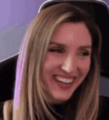 a woman with long blonde hair is smiling while sitting in a gaming chair .