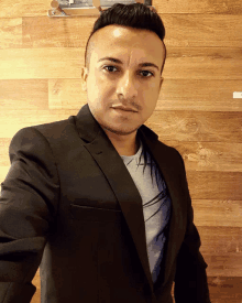 a man in a black suit stands in front of a wood paneled wall