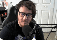 a man wearing glasses and headphones is sitting in front of a microphone with a shirt that says " aul "