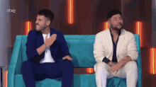 two men are sitting on a blue couch with rtve written on the bottom