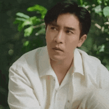 a man in a white shirt is sitting in the woods with his arms crossed .