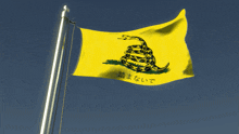 a yellow flag with a snake and a tree on it is flying in the wind against a blue sky