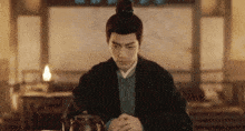 a man in a kimono is sitting at a table with a teapot in his hands .