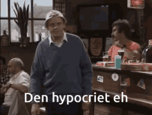 a man in a blue sweater stands in front of a bar with the words den hypocrite eh written on the bottom