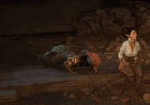 a woman is sitting on a rock next to a river while a man crawls on the ground