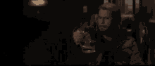 a man with a beard is holding a glass of beer in his hand in a dark room .