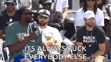 a group of men are sitting in a row and one of them is holding a microphone and talking into it .