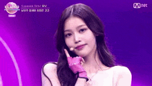 a woman wearing pink gloves and a white top is on a stage with a mnet logo in the background