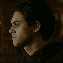 a young man with curly hair is wearing a black hoodie and looking at the camera .
