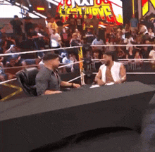 two men are sitting at a table in front of a crowd with a sign that says nxt on it