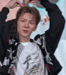 a young man wearing a black jacket and a white t-shirt with the letter m on it is making a heart shape with his hands