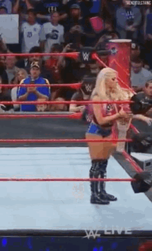 a woman is standing in a wrestling ring with a crowd watching behind her .