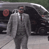 a man in a suit and tie stands in front of a black mercedes van