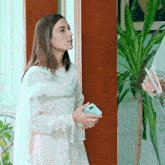 a woman in a white dress is standing in front of a door holding a cell phone