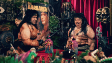 two men in barbarian costumes are sitting in front of a poster for die barbaren