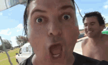a shirtless man making a funny face while another man looks on