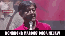 a man in a red shirt is standing in front of a microphone and talking into it .