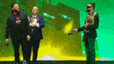 a man wearing a t-shirt that says v8 talks to two other men on a stage