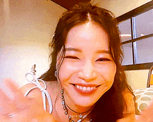 a woman is smiling and waving at the camera while wearing a choker necklace .