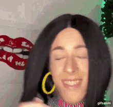 a woman wearing a wig and yellow hoop earrings is smiling with her eyes closed ..