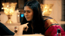 a woman is pointing at another woman while sitting at a table with a bottle of alcohol .