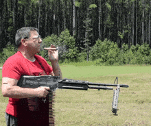 a man in a red shirt smoking a cigar while holding a machine gun