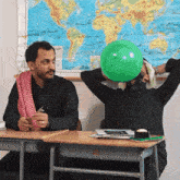 a man blows up a green balloon in front of a world map