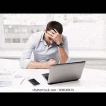 a man is sitting at a desk with his hands on his head in front of a laptop computer .