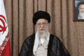 a man with a beard wearing glasses and a turban sits in front of a flag that says ' iran '