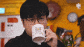 a man wearing glasses is drinking from a mug with a picture of a cat on it