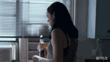 a woman standing in front of a window with a bottle of whiskey in the background and a netflix logo on the bottom