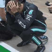 a man is kneeling down with his hands on his head wearing a neos shirt .