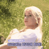 a woman with blonde hair is sitting in the grass with korean writing on the bottom right