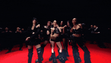 a group of women are standing on a red carpet in a dark room