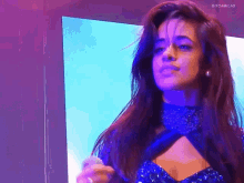 a woman in a blue dress is standing in front of a screen that says gif camilas