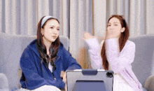 two women sitting on a couch with a tablet