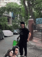 a group of people are standing on a sidewalk with a man holding a green bag