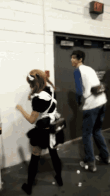 a woman in a maid costume is dancing in front of a red exit sign
