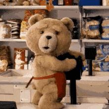 a teddy bear wearing a red apron is standing in front of a cash register .