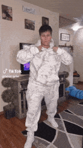 a woman is standing in a living room wearing a white hoodie and white sweatpants