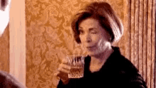 a woman is holding a glass of whiskey and smiling while sitting at a table .