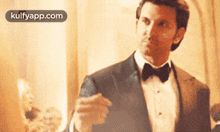 a man in a tuxedo and bow tie is holding a glass of wine in his hand .
