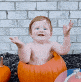 a baby is sitting in a pumpkin with his arms in the air