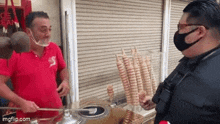 a man wearing a face mask is talking to another man who is selling ice cream .