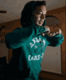 a woman wearing a green eagles sweatshirt is standing in a room