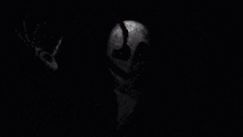 a black and white photo of a skeleton in a suit making a peace sign in the dark .