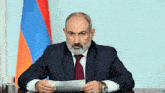 a man in a suit and tie is sitting at a table with a flag in the background