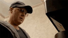 a man wearing glasses and a baseball cap looks down