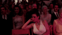 a woman in a white dress and pearls sits in a crowd